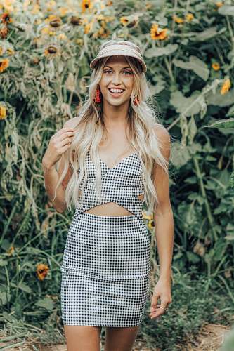 person woman in black and gray checked tank dress stands near sunflower people