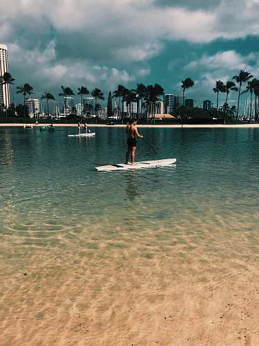 person woman in red dress standing on white surfboard on beach during daytime oars
