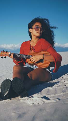 people woman playing ukalele while sitting on gray sand person