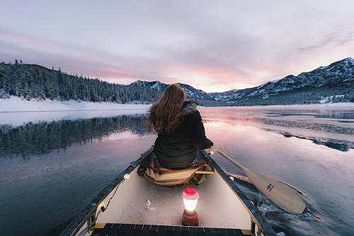 boat woman wearing black winter jacket sitting on boat paddling toward mountains canoe