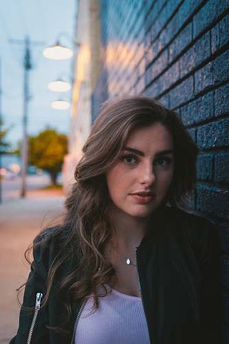 people woman wearing black zip-up jacket leaning on wall person