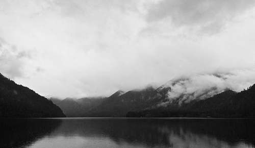 black-and-white mountain covered clouds reflecting on body of water grey