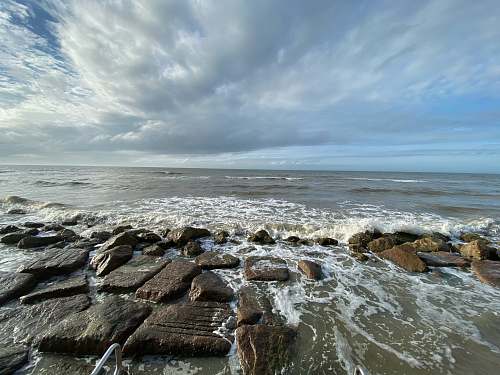ocean brown rocks on sea shore under white clouds and blue sky during daytime outdoors