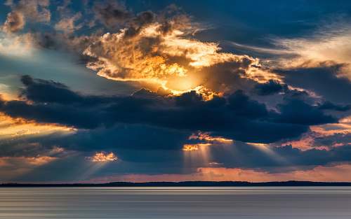 outdoors crepuscular photography of rays from cumulus clouds into the sea sky