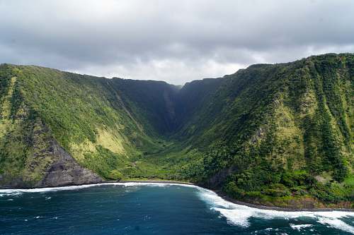 mountain green dense mountain beside body of water under white cloudy sky at daytime cliff