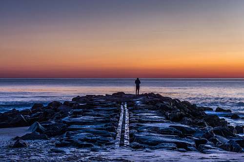 ocean person standing on rocks silhouette coast