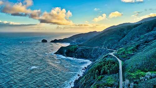 ocean road near a hill and body of water during daytime sea