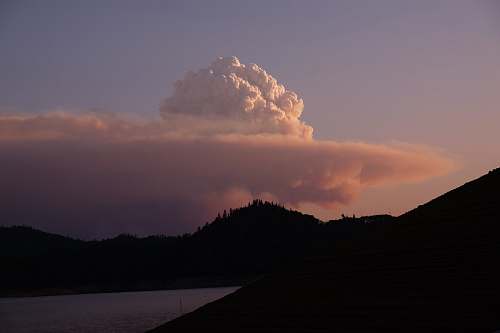 weather silhouette of mountain near body of water during cloudy day outdoors