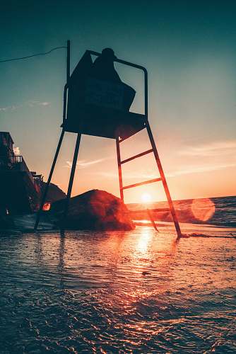 outdoors silhouette photo of person sitting on chair beside sea sunset