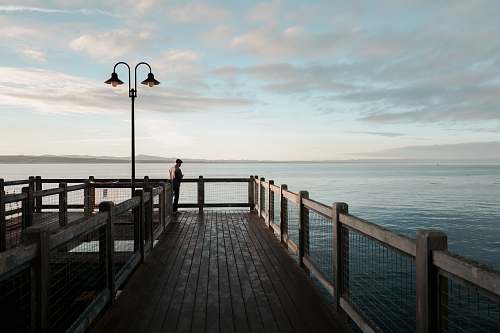 sea man standing on brown dock near lights during daytime pier