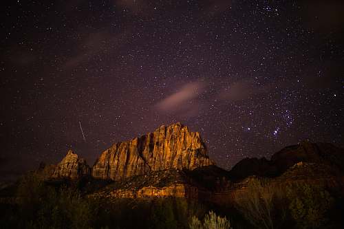 night brown rocky mountain near body of water at night star