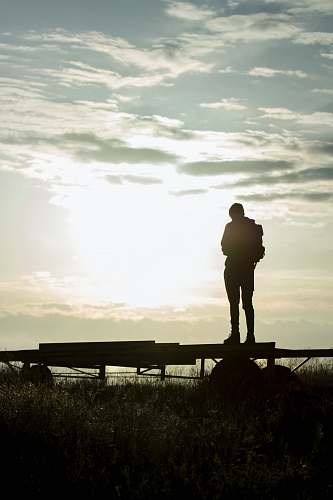 human silhouette of man standing on wooden fence during sunset person