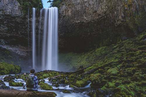 waterfall time-lapse photography of person in front of waterfalls river