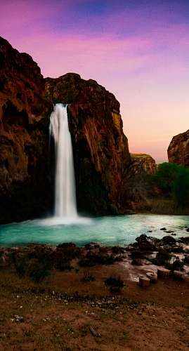 cliff waterfall pouring on body of water rock
