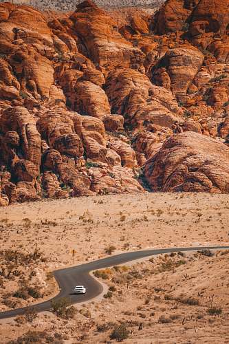 nature white vehicle travelling on curve road surrounded with brown mountains at daytime mountain