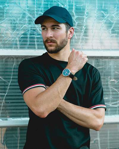 human man wearing black crew-neck shirt and black cap in front of glass wall person