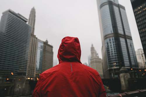 human person wearing red hoodie standing in front of high rise buildings person