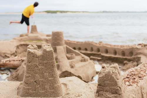 person selective focus photography of sand castle near man standing on seashore human