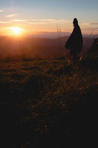 human silhouette photo of person wearing robe standing on hill person
