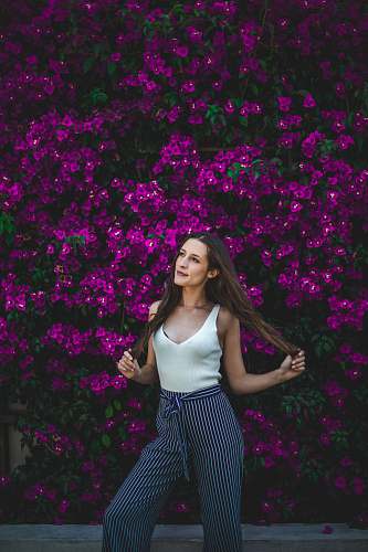 human smiling woman holding her hair in front of purple flowers during daytime person