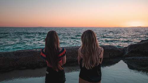 human two woman standing facing body of water during daytime person