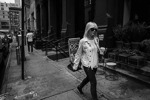person woman walking on pathway near concrete building black-and-white
