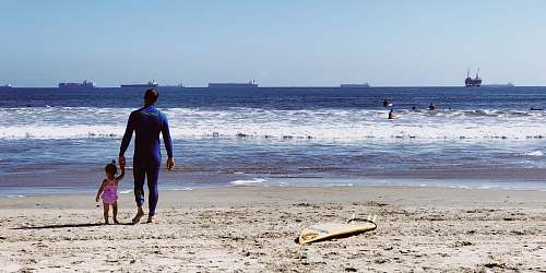 human man holding girl while standing on beach people