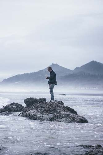 human man standing beside body of water during daytime standing