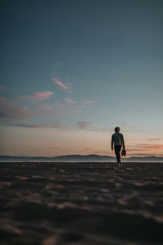 human man walking on sand while holding his footwears people