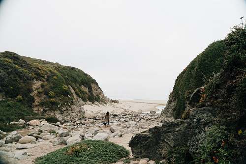 nature person in black shirt standing on brown rock near body of water during daytime outdoors