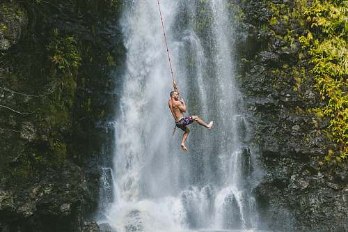 adventure man hanging on rope near waterfalls during daytime bungee