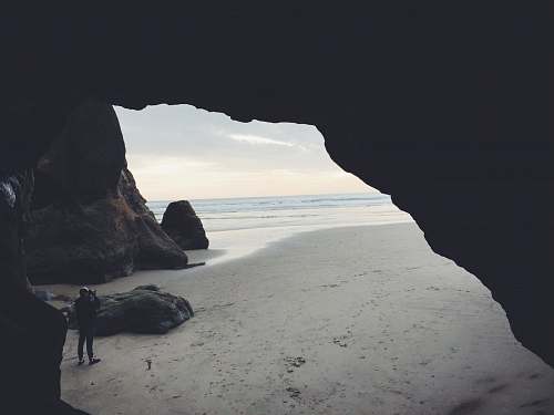 cave person taking picture beside cave ocean