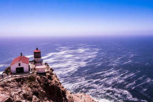 coast white and red shed beside lighthouse on hill overlooking the sea ocean