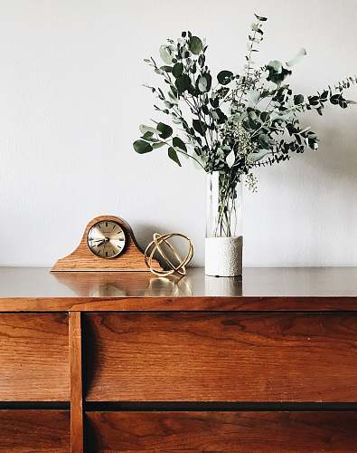 furniture brown wooden framed analog mantle clock near gray petaled flower centerpiece plant