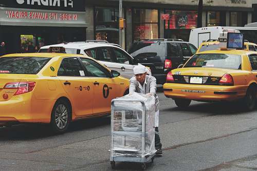 cab man pushing gray bus cart on road near two yellow taxi cabs car