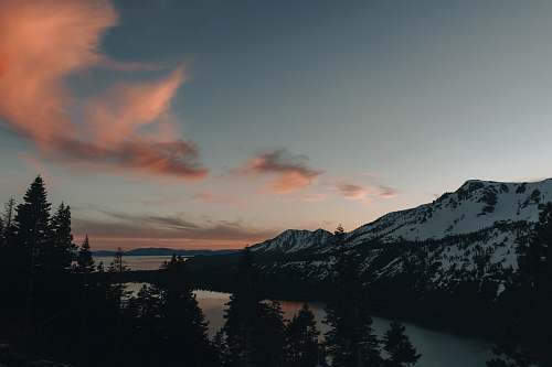 abies body of water within snow-covered mountain range during daytime conifer