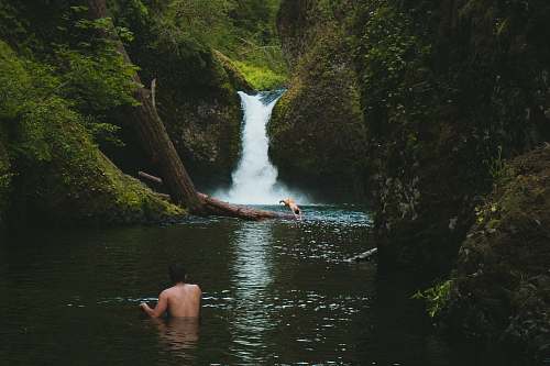 nature person on body of water near waterfalls during daytime forest