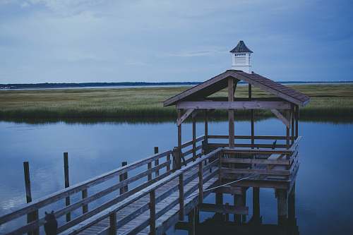 dock gray wooden dock near body of water viewing green rice field under blue and white sky during daytime handrail
