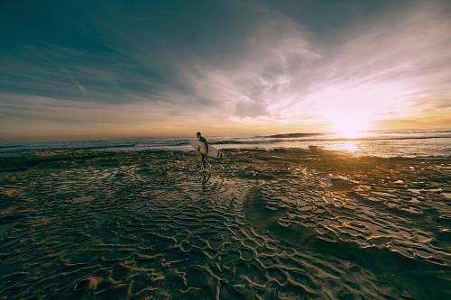 beach man carrying white surfboard while walking on shoreline at daytime san diego