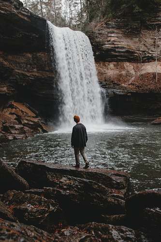 grey man standing on stone facing waterfalls waterfall