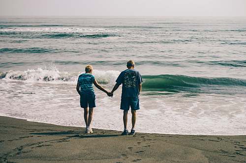 clothing man and woman holding hands together while standing on seashore shorts