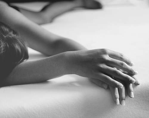 people grayscale photo of person lying on bed hands