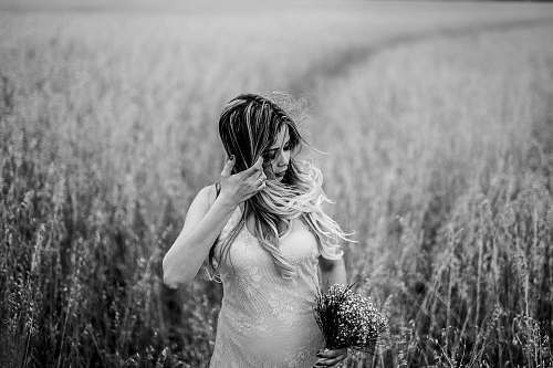 person grayscale photo of woman surrounded by grass wheat