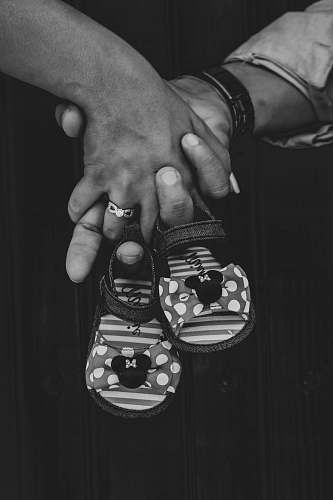 apparel grayscale photography of two person holding hands holding toddler shoes clothing