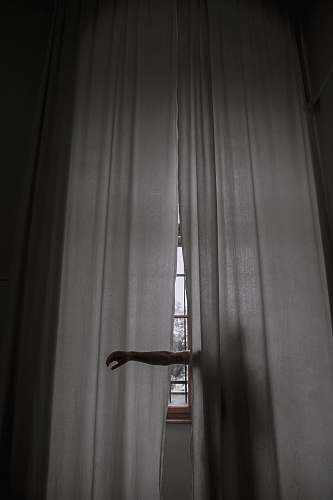 dark person standing beside the curtain and rising their arms grey