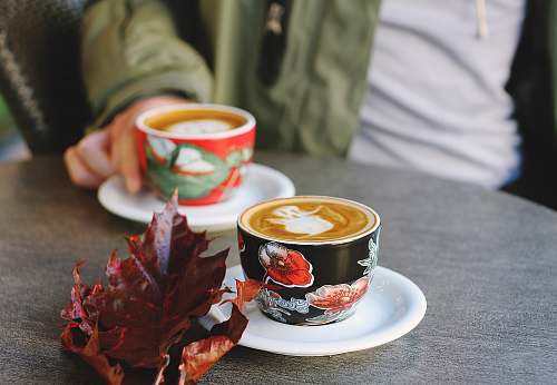 drink selective focus photo of black floral cup on white saucer with latte fall
