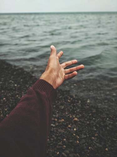 human person raising hand near body of water person