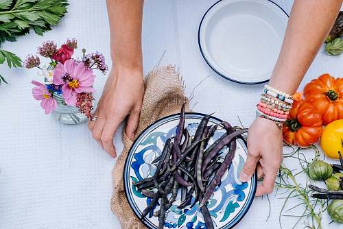 arm person holding white and blue floral ceramic plate with string beans atop near heirloom tomatoes hand