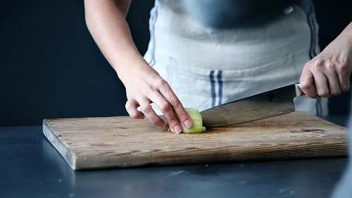 chef person slicing green vegetable on chopping board kitchen