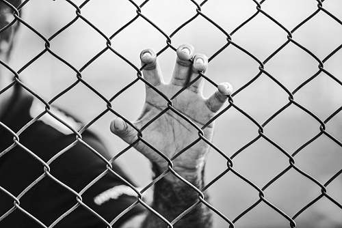 black-and-white man holding chain-link fence prison